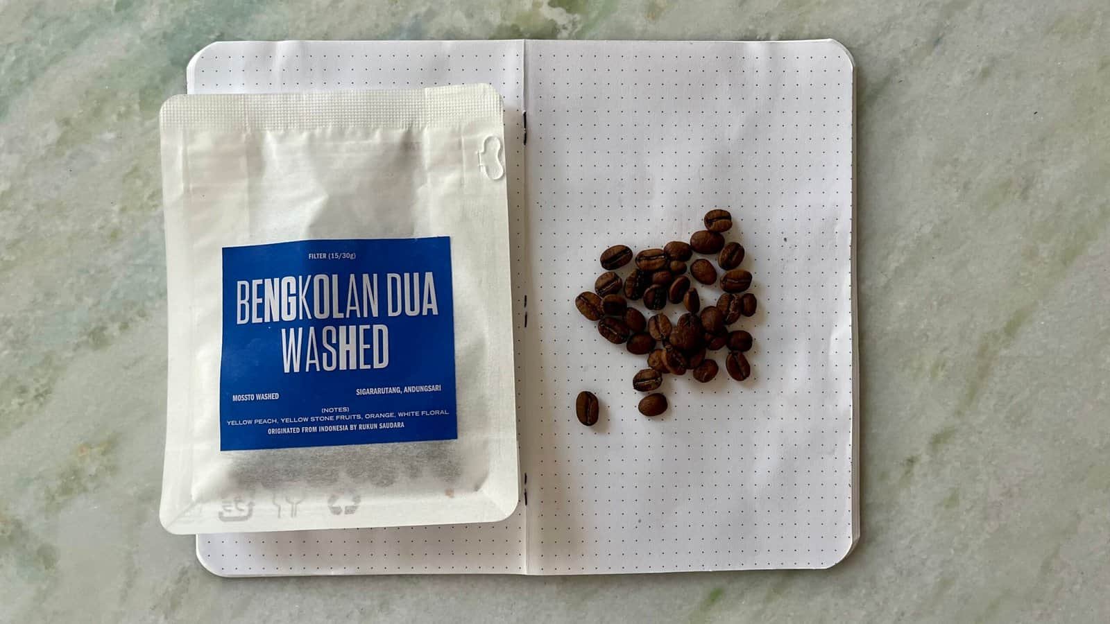 Roasted coffee beans on dotted notebook page with Indonesian coffee packaging, close-up.