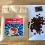 Rich roasted coffee beans and Cherry Apple Bomb seed packet on a wooden surface; perfect for coffee and gardening enthusiasts.