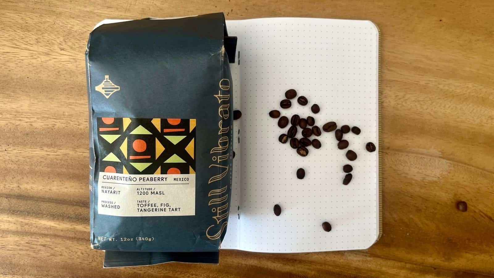 Rich coffee beans from Cuarenteño Peaberry Mexico, on a notebook with scattered beans, showcasing premium quality coffee aligned with Barnaby Robson's coffee expertise.