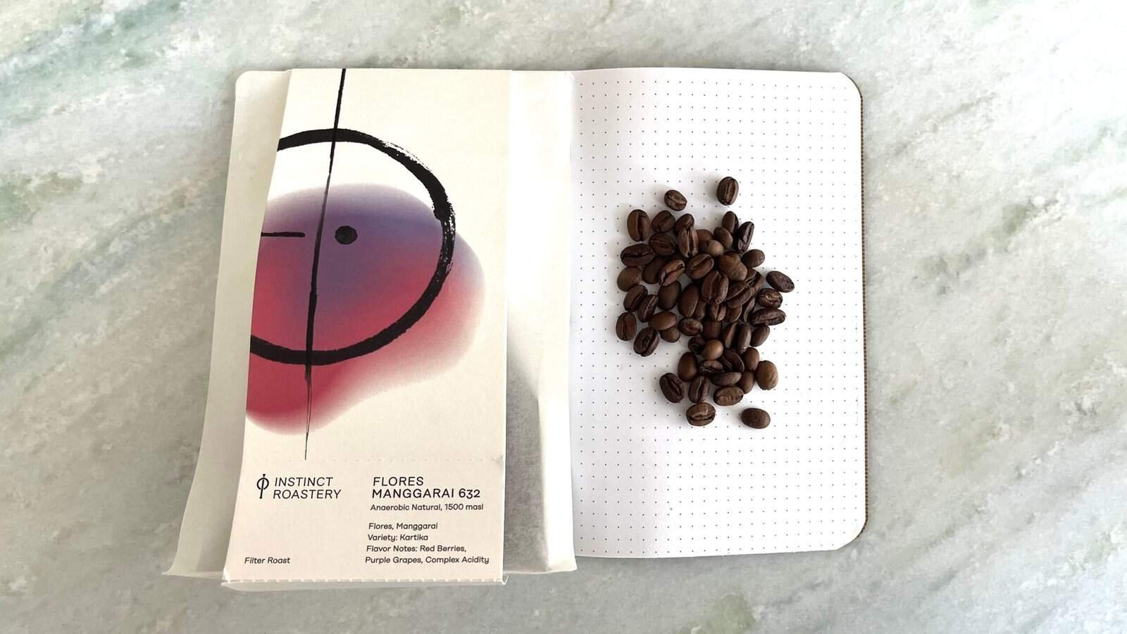 High-quality coffee beans on a dotted notebook page, with colourful abstract art on a paper bag from Instinct Roastery; perfect for coffee lovers and specialty coffee enthusiasts.