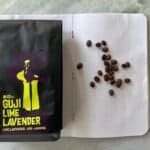 Rich dark roast coffee beans with Guji Lime Lavender branded packaging on a white dotted notebook. Coffee beans are spread out on the notebook, highlighting speciality coffee from Guji, Ethiopia.