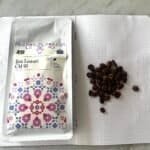 Rich coffee beans and a package of Ijen Lestari CM 91 specialty coffee, on an open dotted notebook, highlighting premium single-origin coffee for connoisseurs.