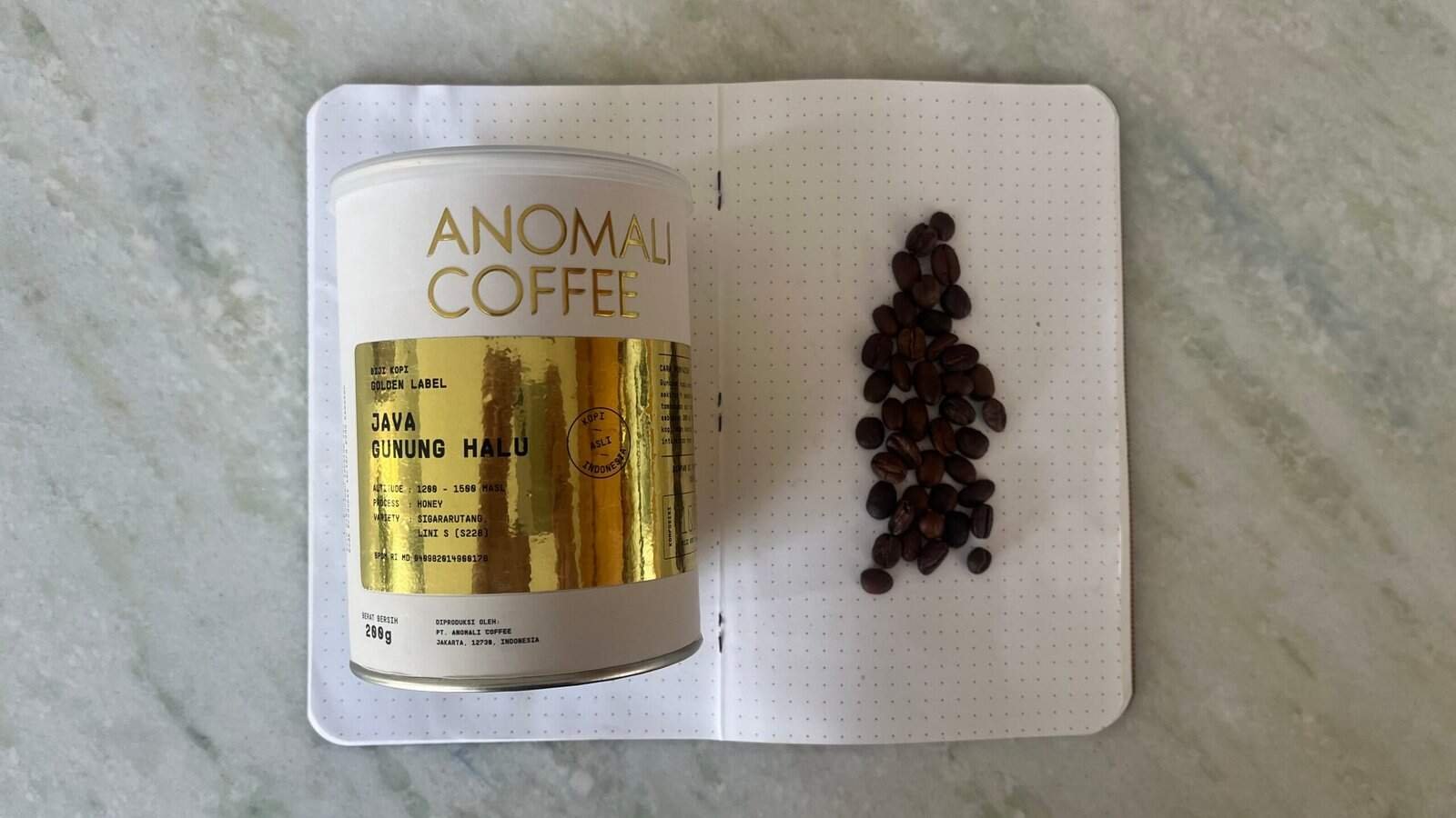 Rich Indonesian coffee beans on a dotted notebook with Anomali Coffee tin, showcasing premium Java Gunung Halu coffee for espresso enthusiasts and coffee connoisseurs.