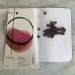 Rich coffee beans on a white dotted notebook with a colourful abstract art card, representing premium coffee and roasting expertise. Perfect for coffee enthusiasts and specialty coffee branding.
