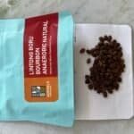 Rich, dark roasted coffee beans spilled from a resealable bag onto a white dotted surface, showcasing high-quality speciality coffee for coffee enthusiasts and connoisseurs, perfect for artisanal brewing.
