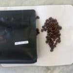 Flash roasted coffee beans on a dotted notebook next to a black sealed bag labelled "Puntang Natural" with a date label for January 25th.