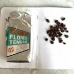 Freshly roasted Seniman Flores Tengah coffee beans and a bag of processed coffee on an open notebook. Perfect for coffee enthusiasts and quality coffee sourcing.