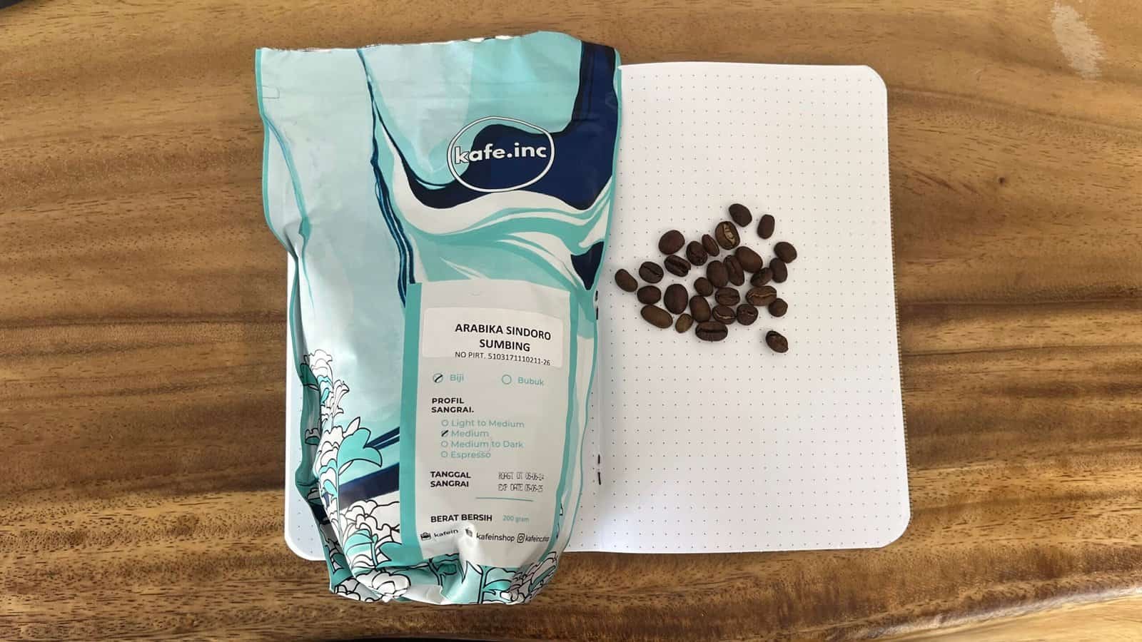 Fresh Arabika Sindoro Sumbing coffee beans on a notebook with a wooden table background, highlighting high-quality single-origin coffee for brewing and tasting enthusiasts.