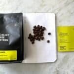 Bright yellow and black coffee packaging with roasted coffee beans on a white dotted notebook, showcasing premium Indonesian Blacklist coffee beans, highlighting speciality coffee beans and sustainable sourcing.