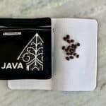Coffee beans scattered on dotted notebook next to a black Java programming book with an intricate design.