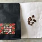 Rich coffee beans on dotted notebook page with black packaging labelled "Strawberry Fields" from Space Roastery, ideal for speciality coffee lovers and online coffee shop branding.