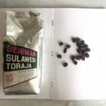 Freshly roasted Sulawesi Toraja coffee beans on a dotted notebook page with the packaging beside them. High-quality, medium roast Arabica coffee beans ideal for brewing a rich, aromatic coffee experience.