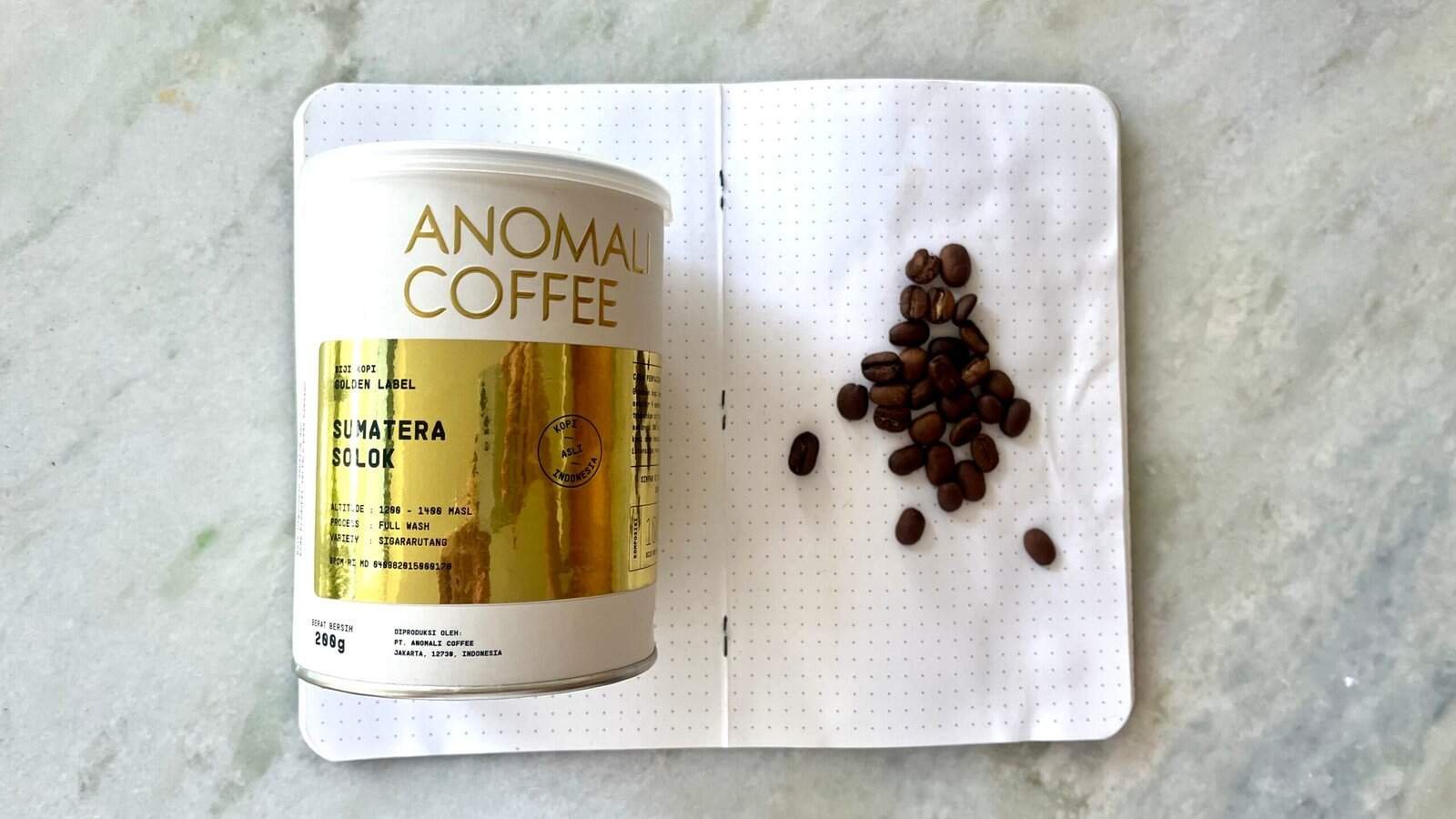 Roasted Sumatran coffee beans and a branded coffee tin on an open notebook, showcasing premium Indonesian coffee quality and specialty coffee beans for coffee lovers.