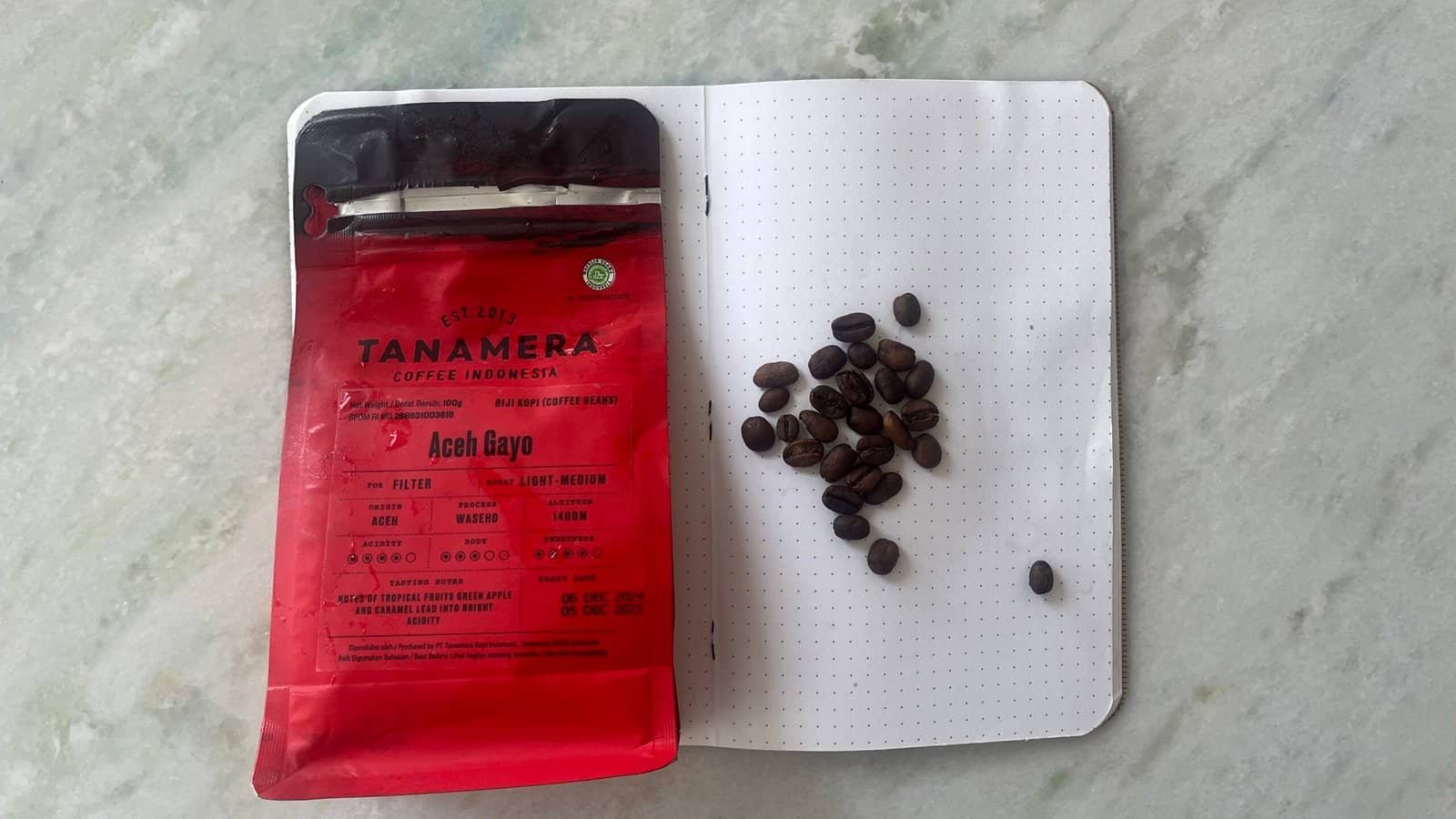 Rich coffee beans from Aceh Gayo Indonesia with brewing notes on a notebook. Coffee lover’s guide to high-quality Arabica beans, featuring Tanamera Coffee Indonesia, showing freshly roasted coffee beans on a textured surface.