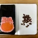 Rich coffee beans and a bag of "The Pink Mandarín" speciality coffee on a notebook with coffee beans arranged in a pattern, showcasing premium coffee roasting by Barnaby Robson.