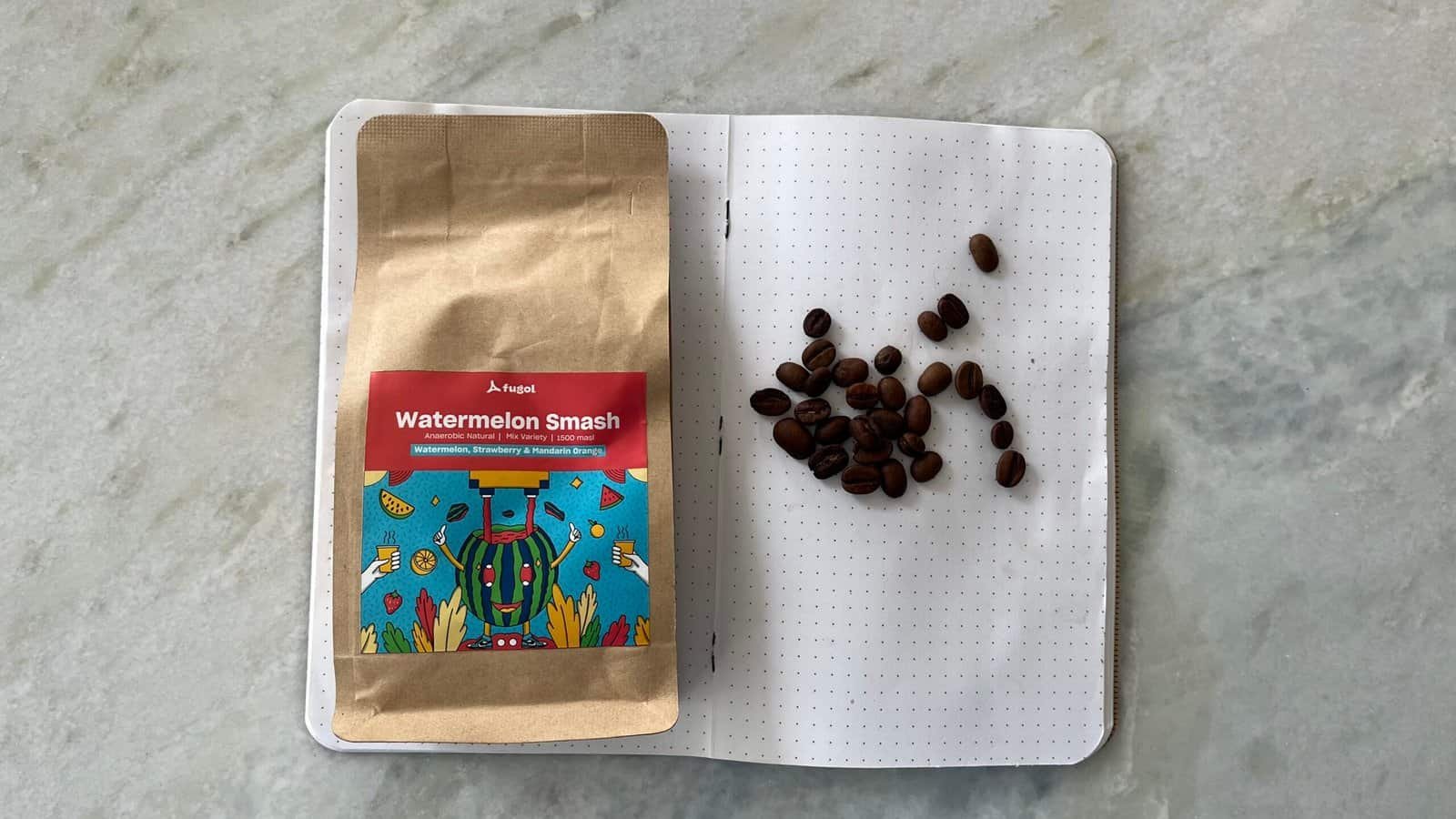 Rich coffee beans and a colourful watermelon smash herbal tea package on a white dotted notebook.
