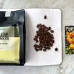 Dark roasted Yellow Caturra coffee beans from East Nusa Tenggara, Indonesia, displayed on a notebook with a colourful coffee farm card for organic coffee lovers.